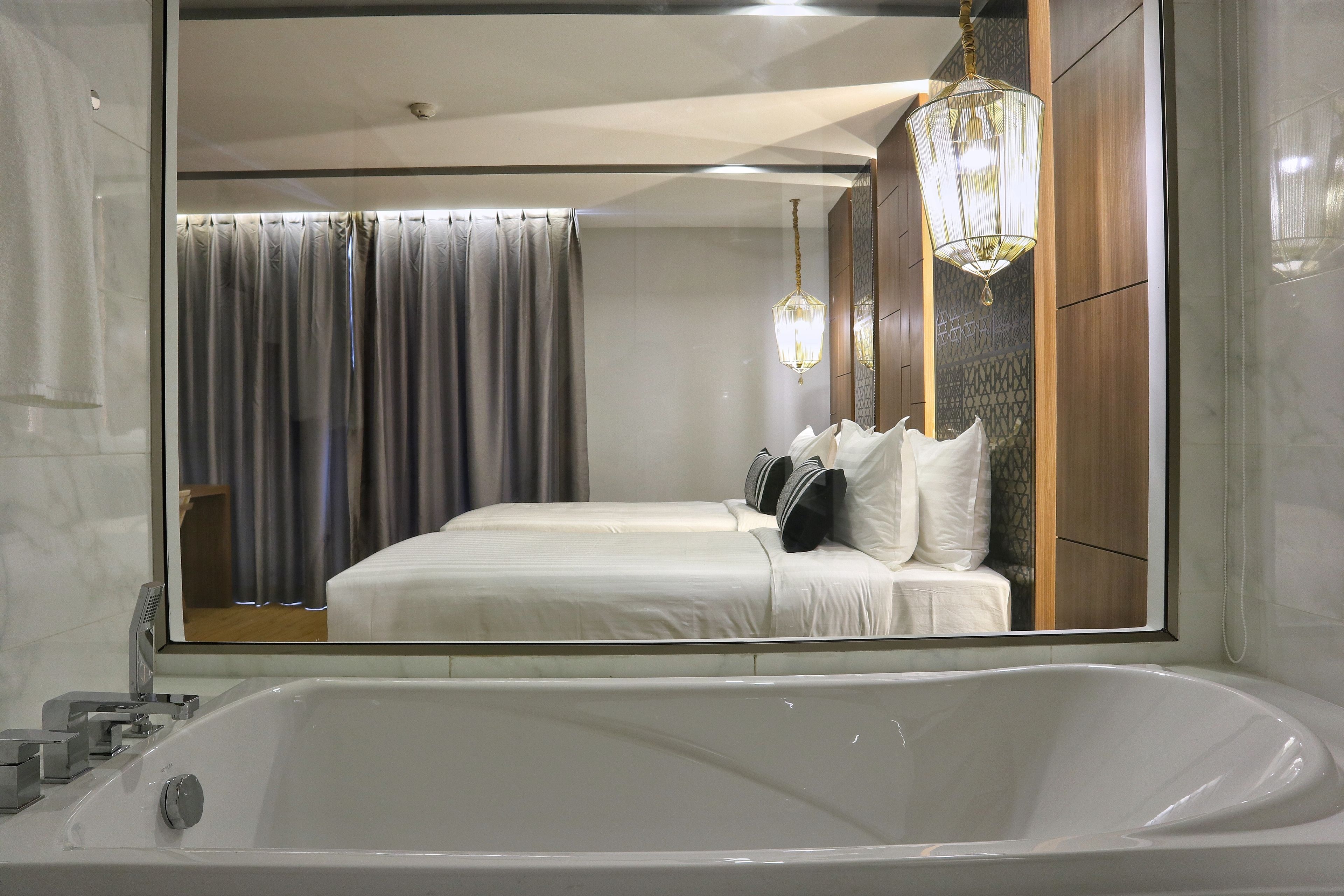A modern hotel room with a large bed, a bathtub, and a mirror reflecting the room.