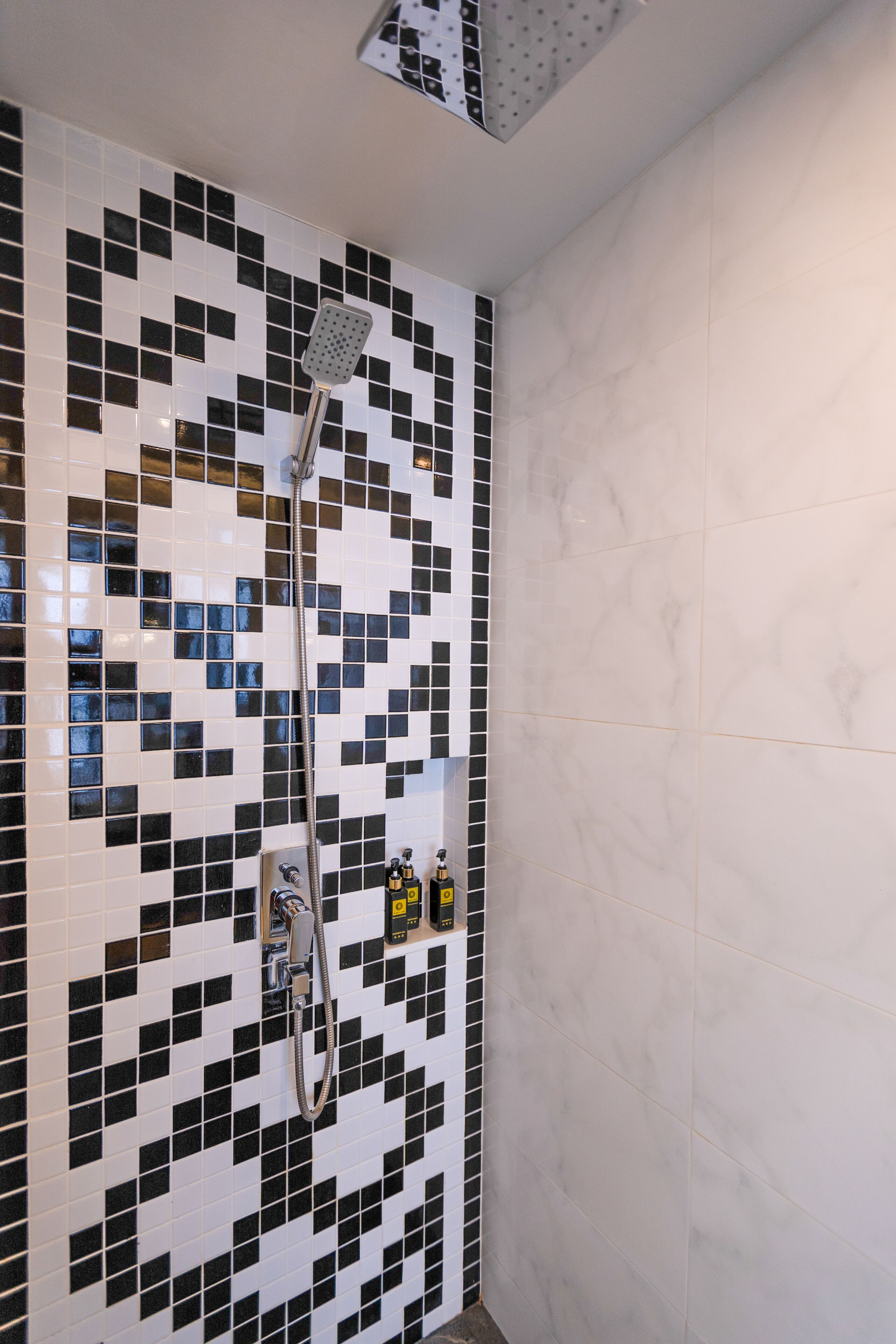 Ducha con pared de mosaicos blanco y negro, cabezal de ducha de mano y panel de control instalado en la pared.
