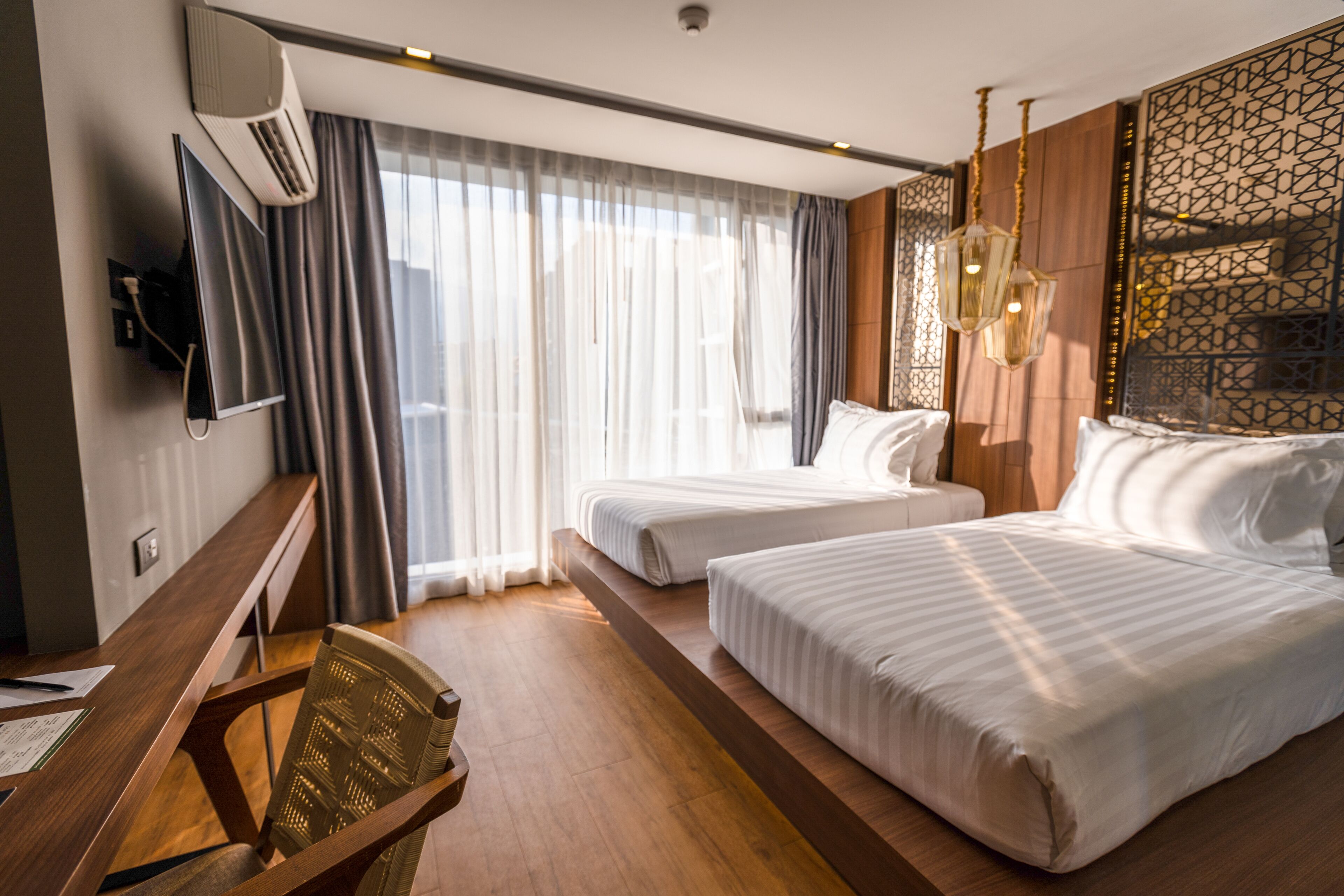 Habitación de hotel con dos camas, un escritorio con silla, televisión de pantalla plana y un ventanal con cortinas.