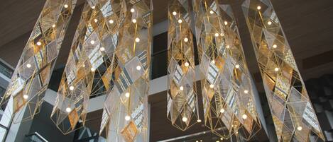 A modern interior with geometric hanging light fixtures and a glass railing on a balcony.