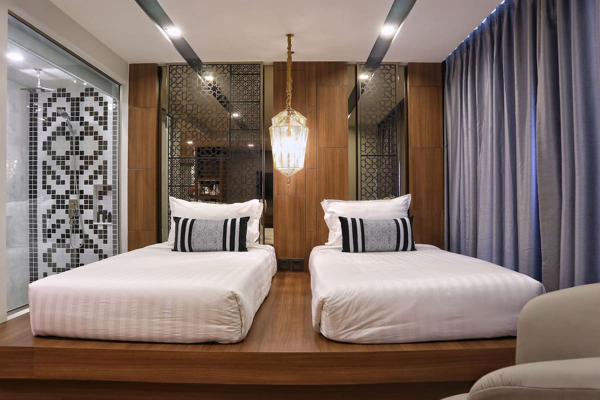 A modern hotel room with two beds, a chandelier, and a large mirror.