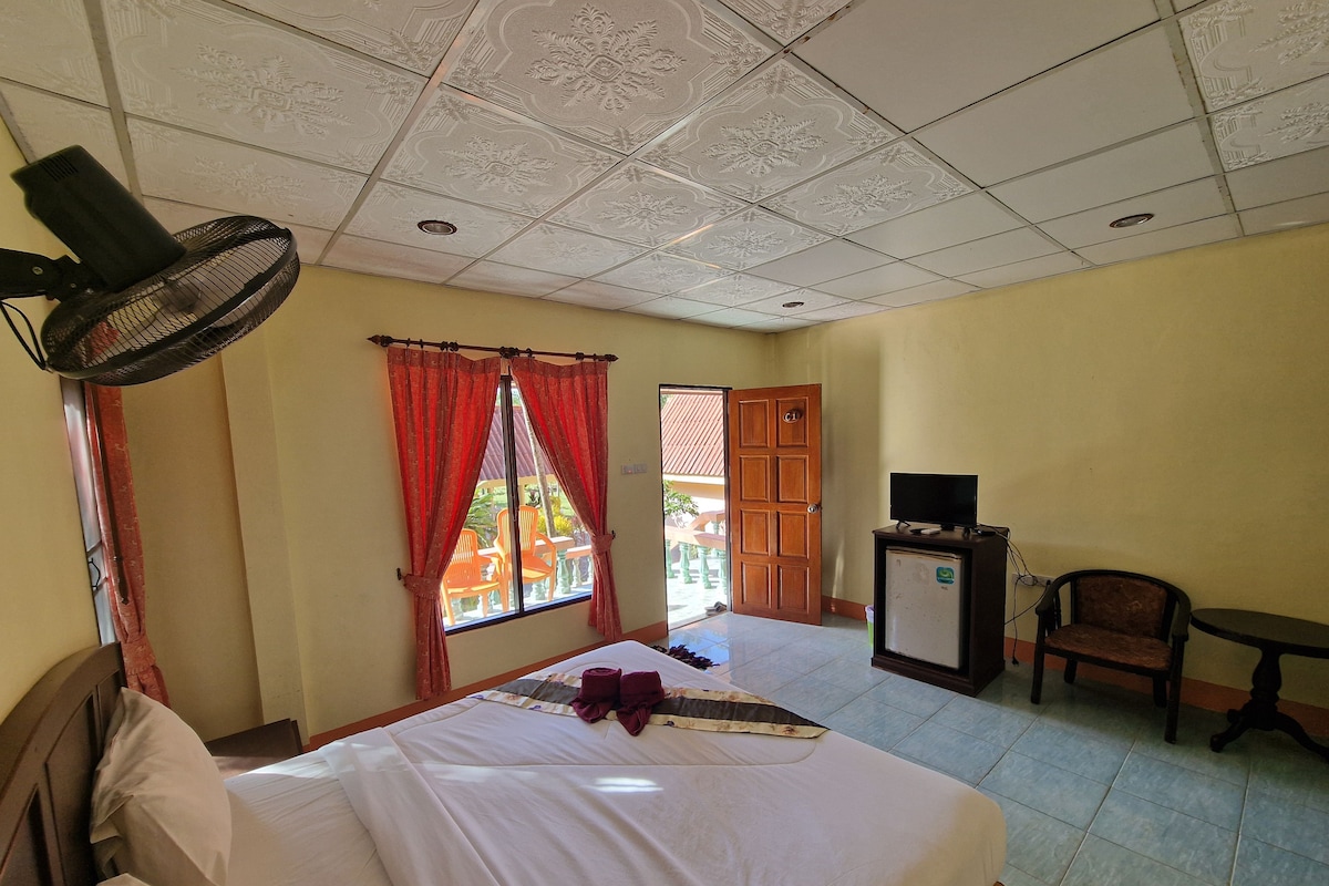 A hotel room with a bed, a TV, a chair, and a fan.