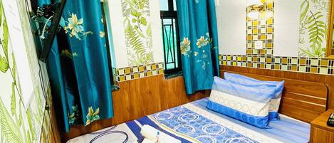 A neatly arranged bedroom with a bed, a bedside table, a fan, and a window with curtains.