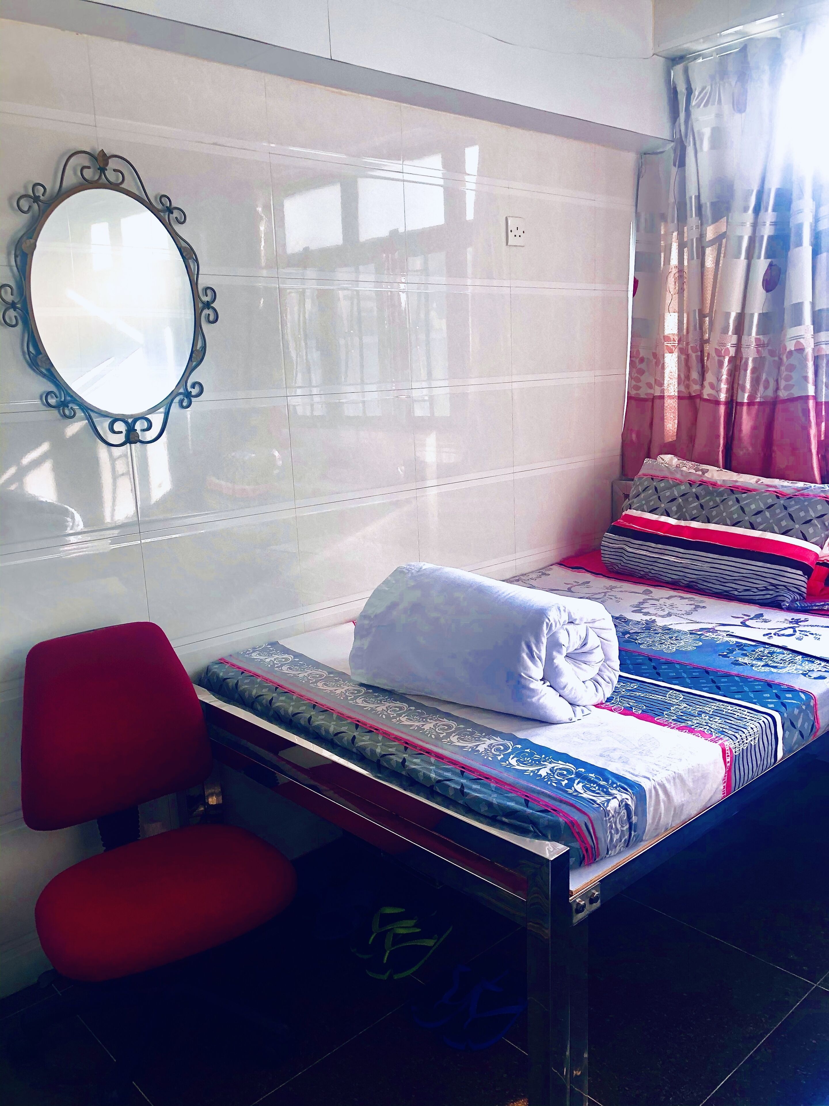 A hotel room with a bed, a red chair, a small table, and a mirror on the wall.