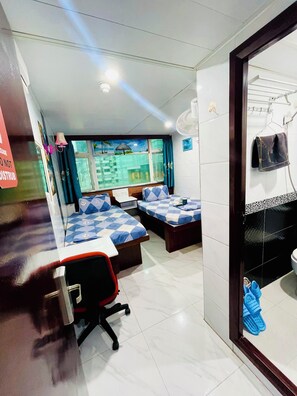 A hotel room with two beds, a desk, a chair, a window with a view of buildings, and a bathroom with a sink and toilet. - Kyoto Guest House (Kowloon)