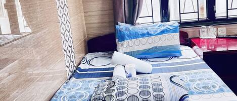 A neatly made bed with patterned bedding, a wall-mounted lamp, and a window with curtains.