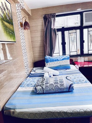 A neatly made bed with patterned bedding, a wall-mounted lamp, and a window with curtains. - Kyoto Guest House (Kowloon)