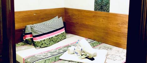 Una habitación pequeña y ordenada con una cama, una mesita de noche, una lámpara y un panel decorativo en la pared junto a un cuadro enmarcado.