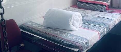 Un dormitorio pequeño y ordenado con cama, una silla, un espejo y una ventana con cortinas.