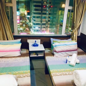 A hotel room with two beds, a small table, and a view of a cityscape at night. - Kyoto Guest House (Kowloon)