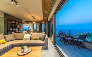 Una sala de estar moderna con un amplio sofá modular, un comedor con sillas de madera y vistas al océano.