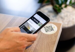 Un smartphone affichant l’interface d’une application de réservation d’hôtel, avec un code QR visible sur une surface en bois.