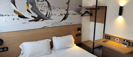 A hotel room with a bed, a nightstand, a wall-mounted lamp, and a painting.