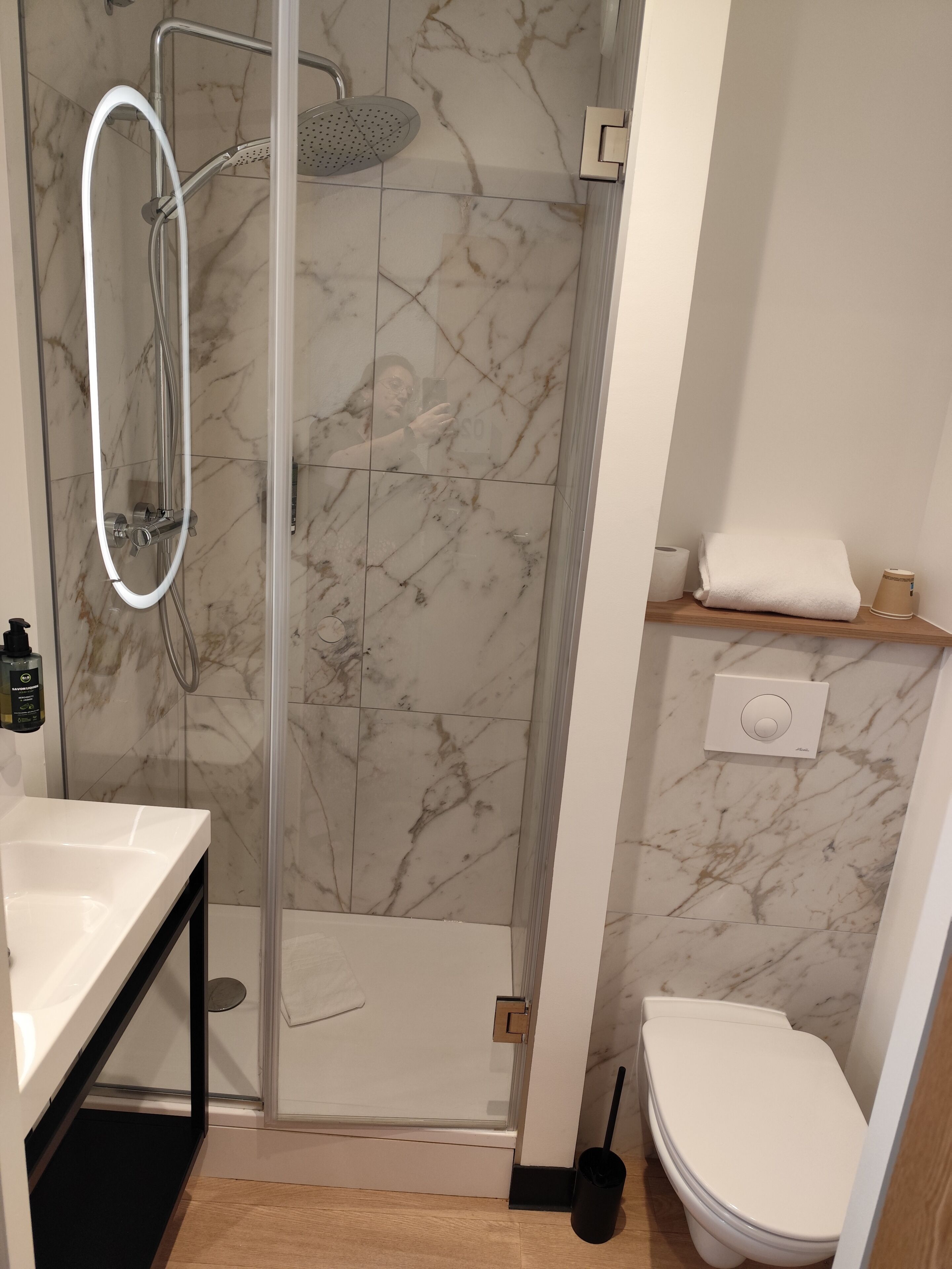 Un baño moderno con ducha envuelta en vidrio, inodoro blanco y pared con azulejos de mármol.
