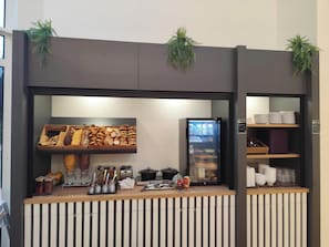 Una estación de desayuno autoservicio con diversos pasteles, salsas y un mostrador refrigerado.