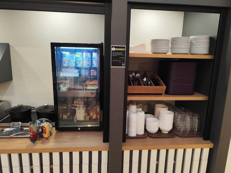 A self-service breakfast station with a refrigerator, condiments, and utensils.
