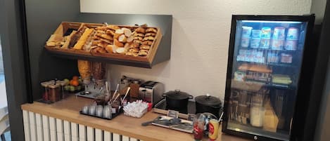 Mostrador de comidas con una exhibición de pasteles, una máquina de café y un refrigerador.