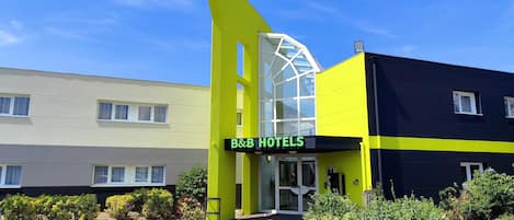 Un hotel tipo casa de huéspedes con diseño moderno, que destaca por su fachada amarilla y negra, una entrada de vidrio y un estacionamiento.