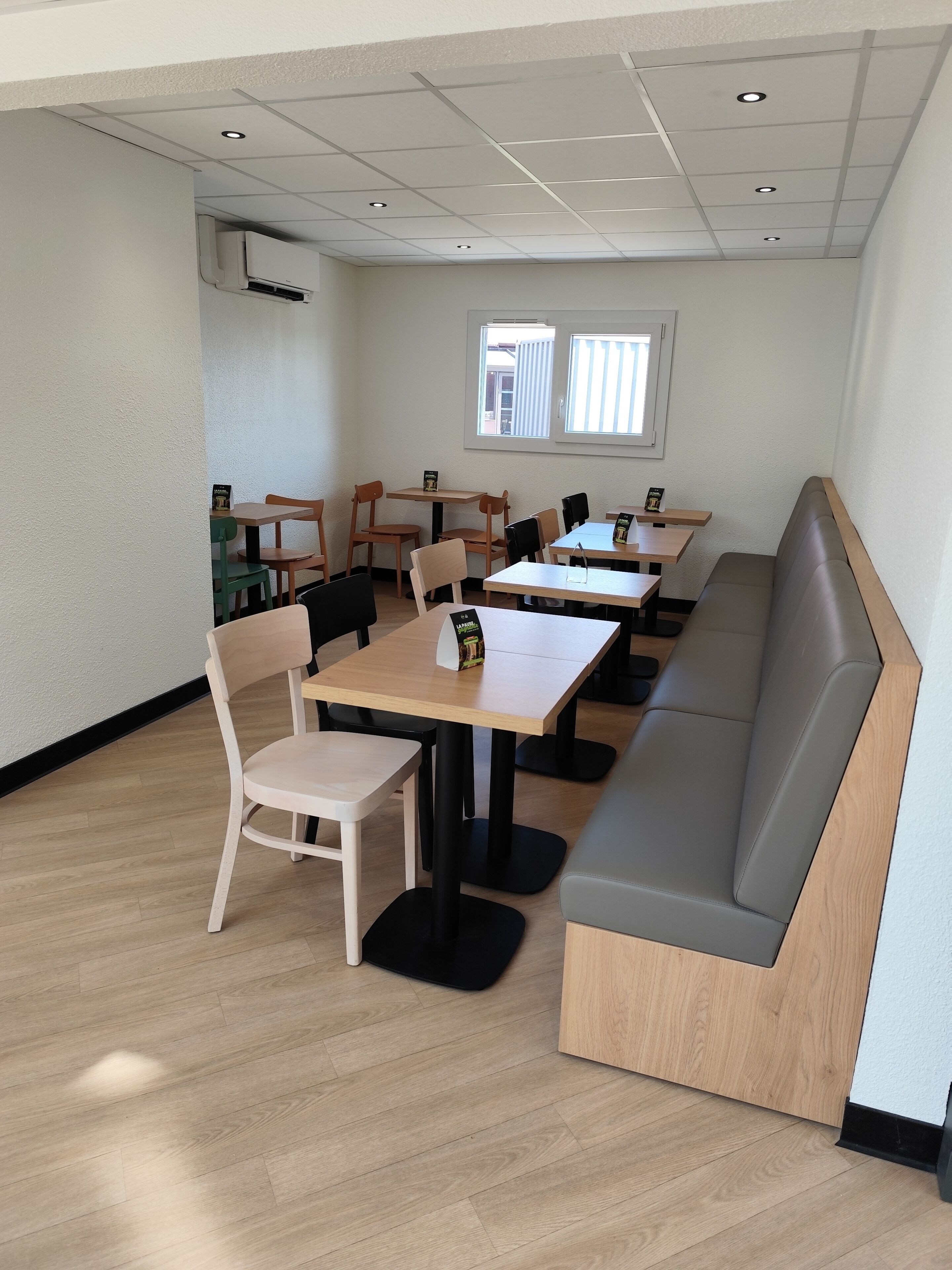 Un comedor moderno con mesas y sillas de madera, un banco y un ventanal que proporciona luz natural.