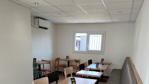 Een moderne eetruimte met houten tafels en stoelen, een bankje en een raam dat natuurlijk licht binnenlaat.