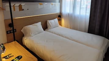 A hotel room with a bed, a nightstand, a wall mural, and a window with curtains.