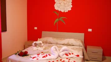Une chambre d’hôtel avec un mur rouge, un lit recouvert d’une courtepointe à motifs floraux, une table de chevet et une décoration murale représentant une fleur et un cygne.