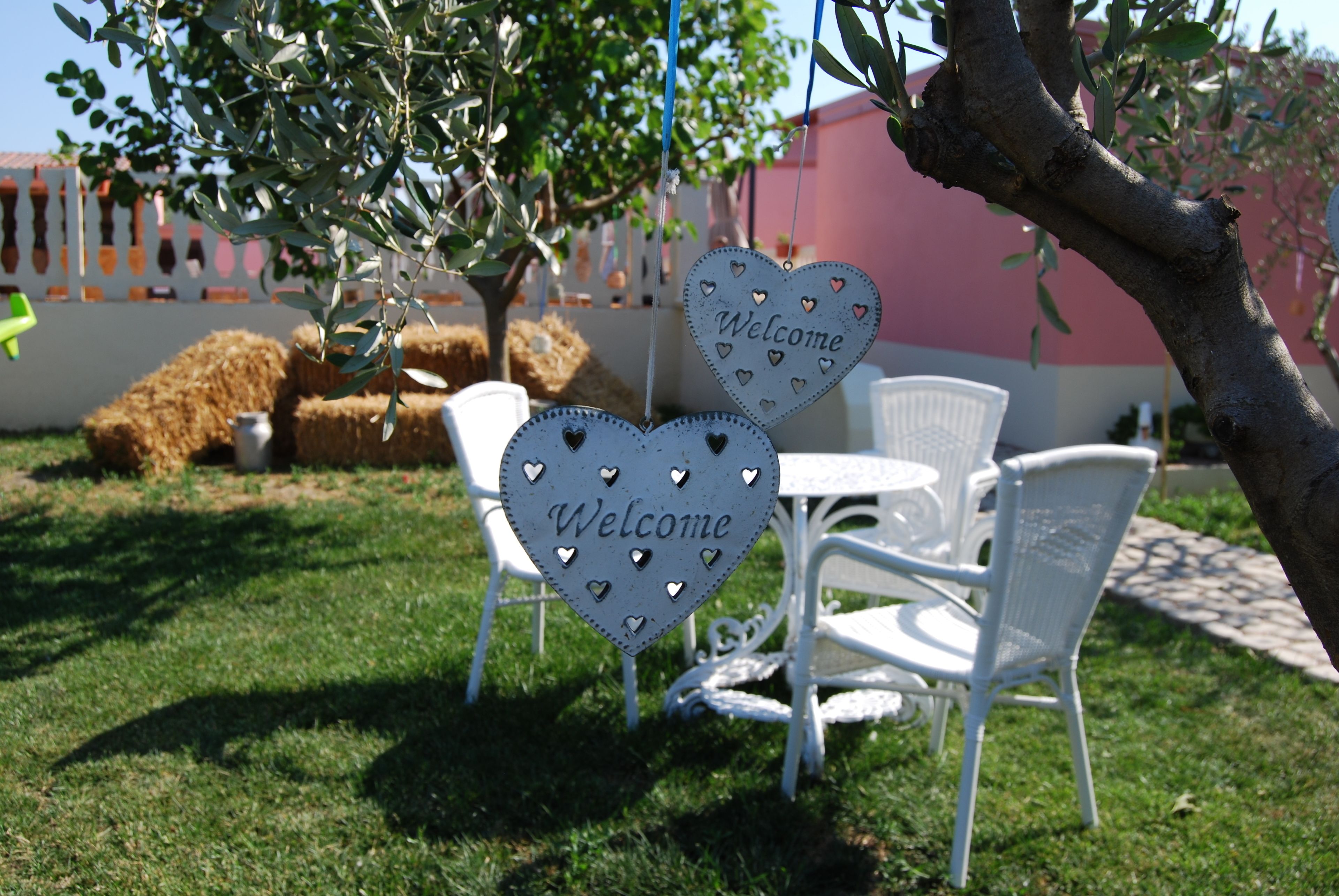 A garden area with two white chairs and a small table, surrounded by a white fence and hay bales.