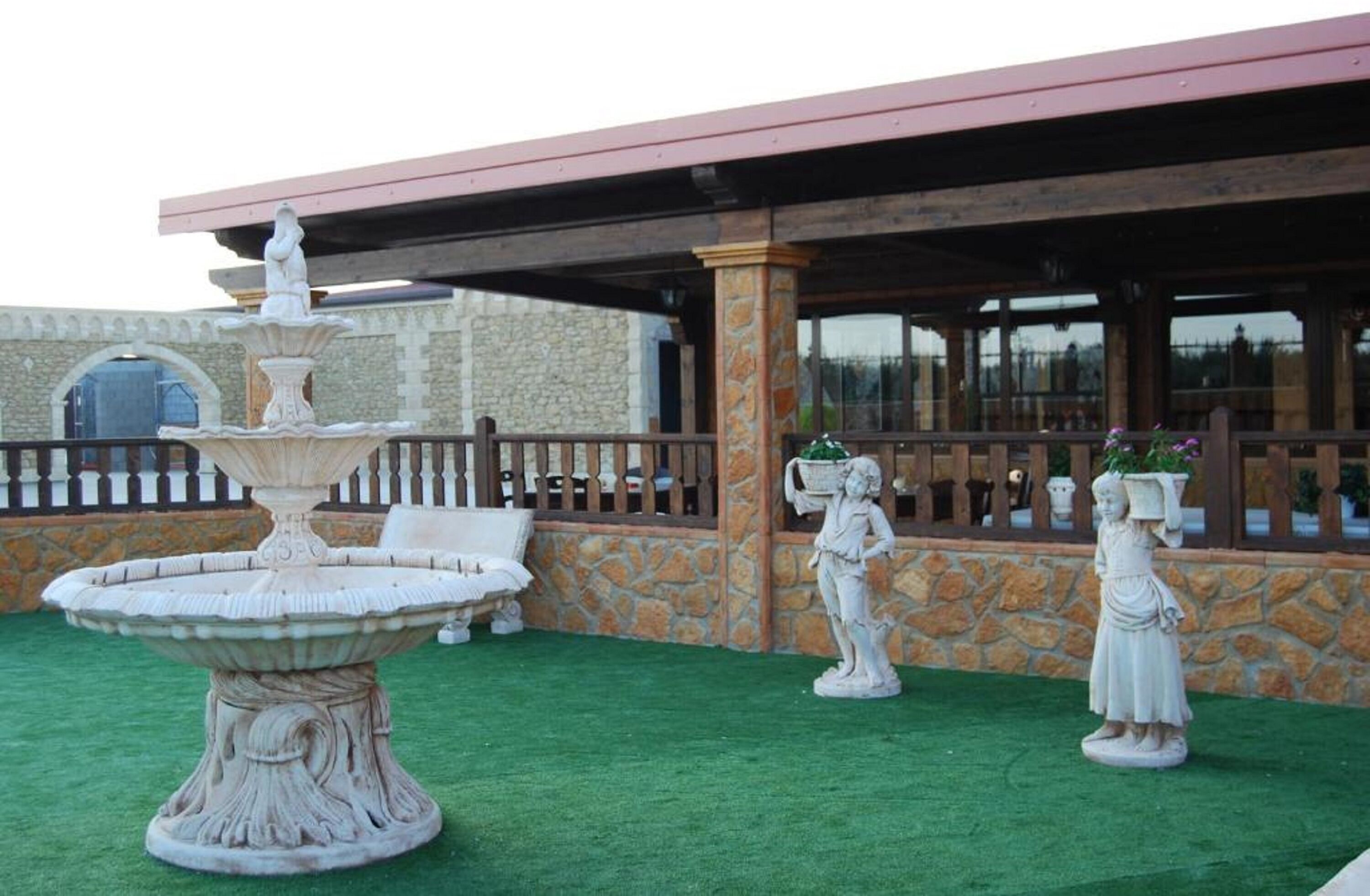 Un patio con una fuente de piedra, estatuas y un área de estar cubierta.