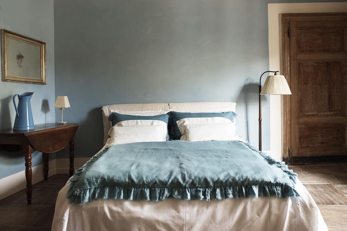 A bedroom with a bed, a nightstand, a lamp, a wooden door, and a framed picture on the wall.