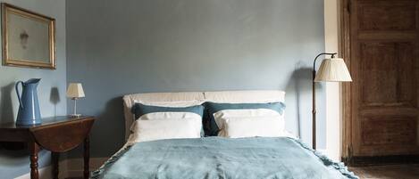 A bedroom with a bed, a nightstand, a lamp, a wooden door, and a framed picture on the wall.