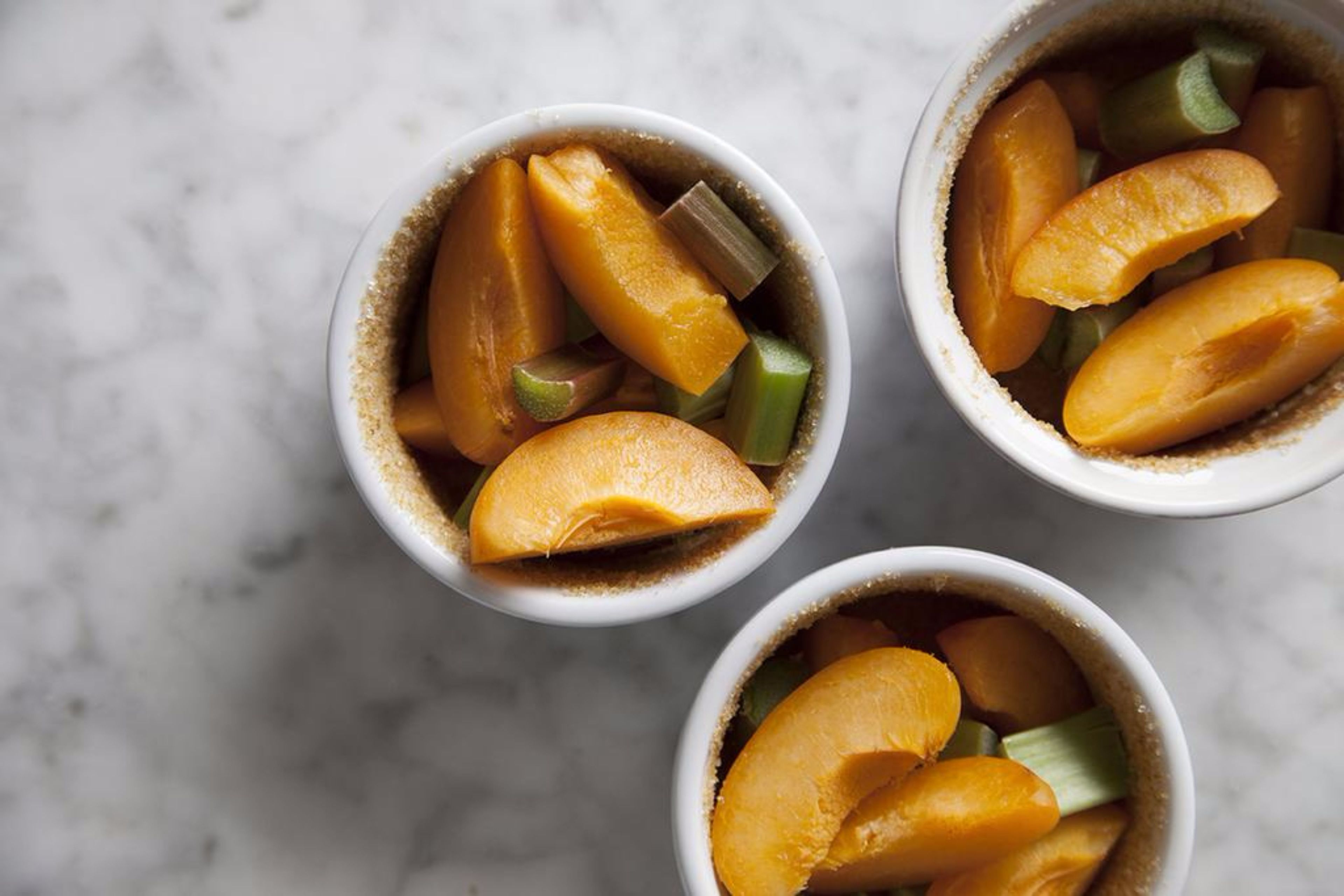 Three bowls containing sliced fruits on a marble surface.