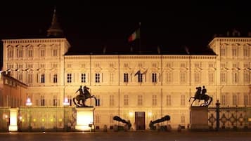 A large, illuminated building with classical architecture, featuring statues and a prominent entrance.