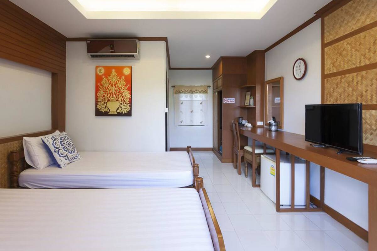 A hotel room with a bed, a desk with a television, a clock, and a bathroom door.
