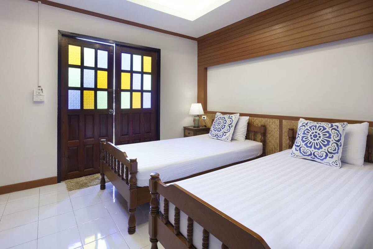 A hotel room with two beds, wooden headboards, a nightstand with a lamp, and a large window with a view of the outside.
