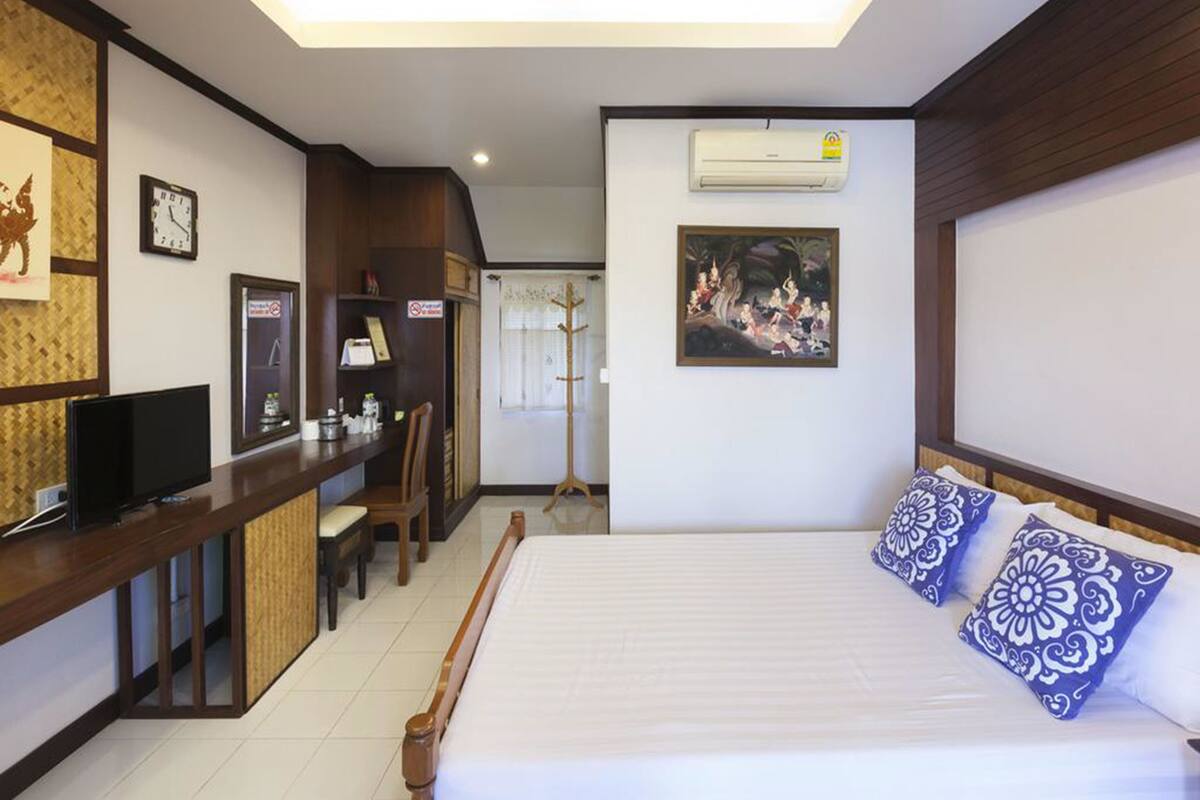 A hotel room with a bed, a desk with a television, a clock, and a painting on the wall.