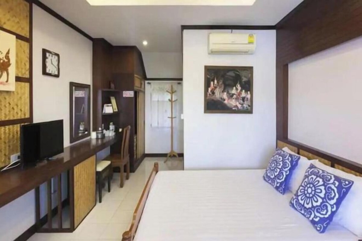 Una habitación de hotel con cama, escritorio con televisor, silla y perchero.