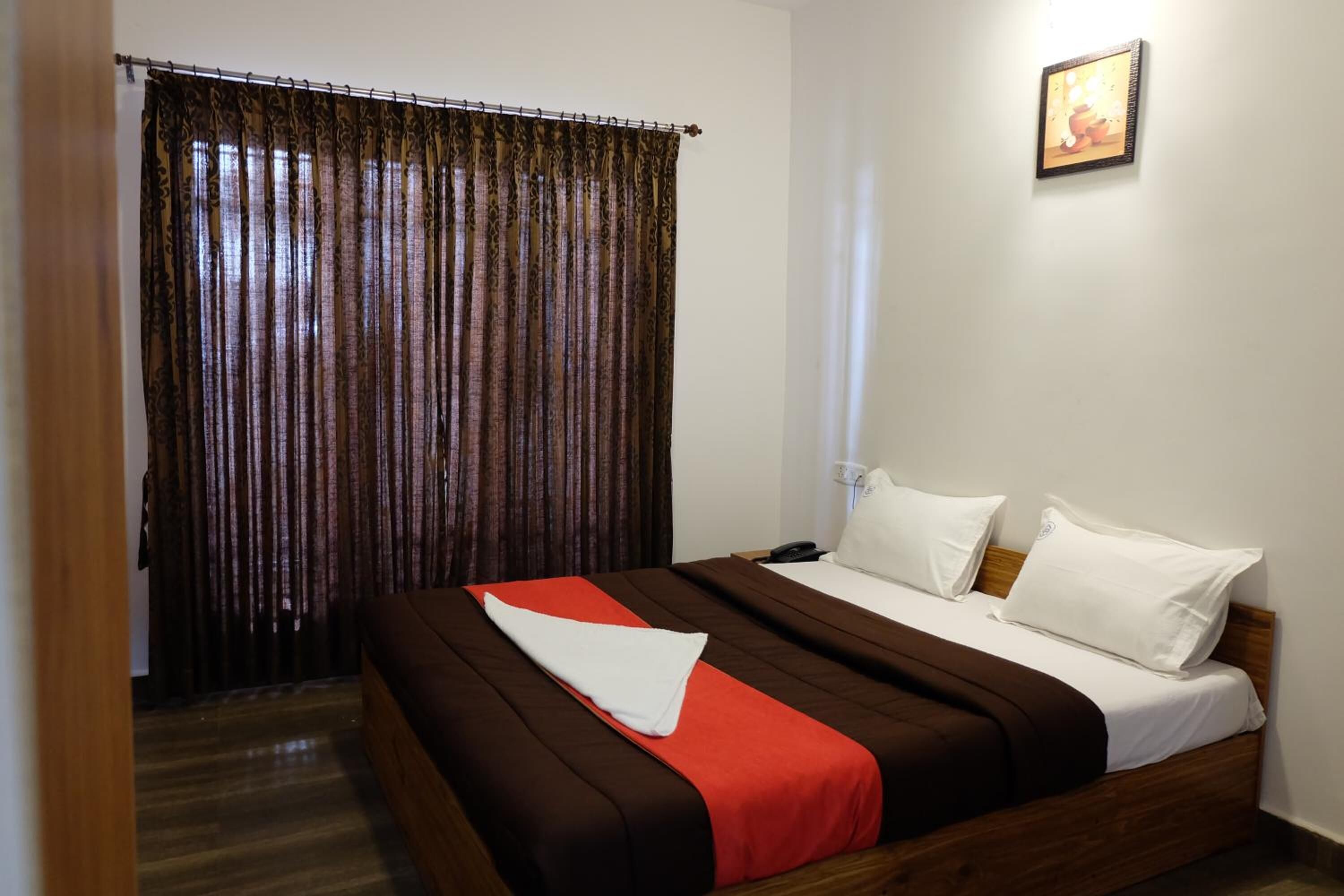 Camera d'albergo con un letto di legno, cuscini bianchi, una coperta rossa e un tendaggio decorato.