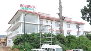 Un immeuble de la résidence Rosepark, avec plusieurs étages, un toit recouvert de tuiles rouges et plusieurs véhicules garés devant.