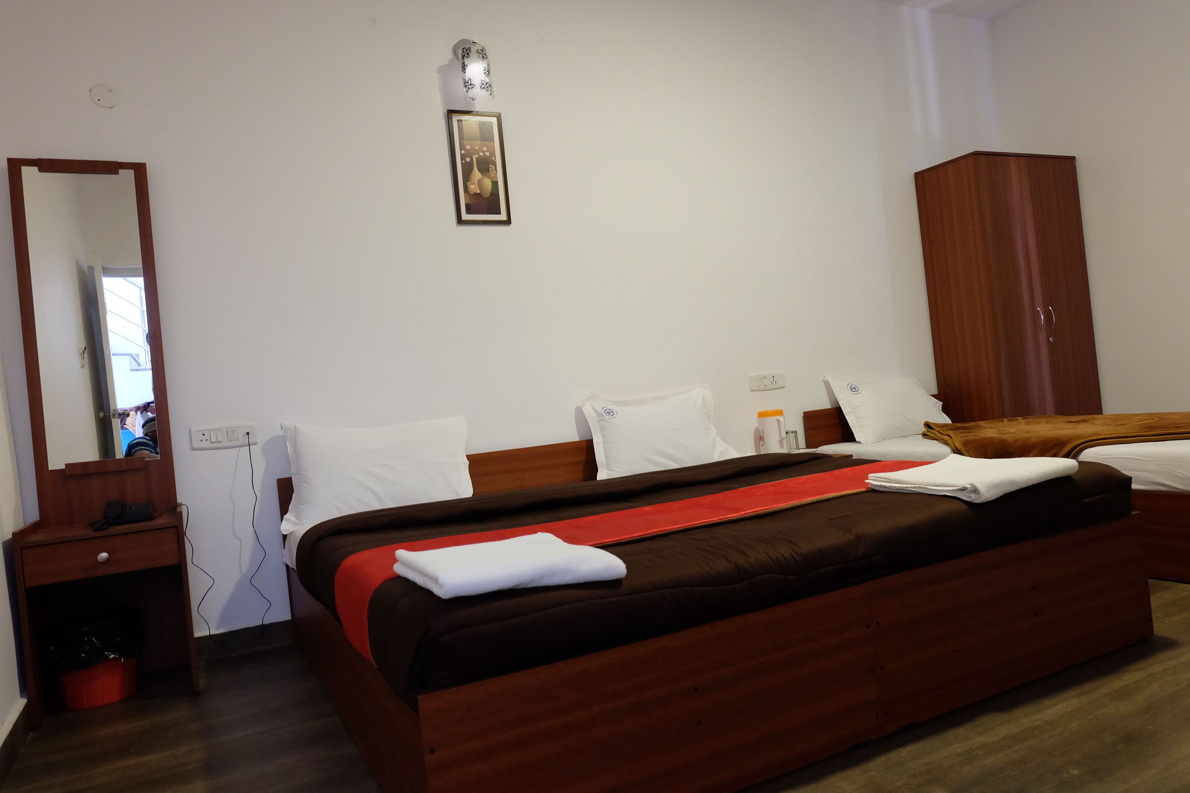 Una habitación de hotel con una cama grande, un armario de madera, una mesita de noche con una lámpara y un cuadro colgado en la pared.
