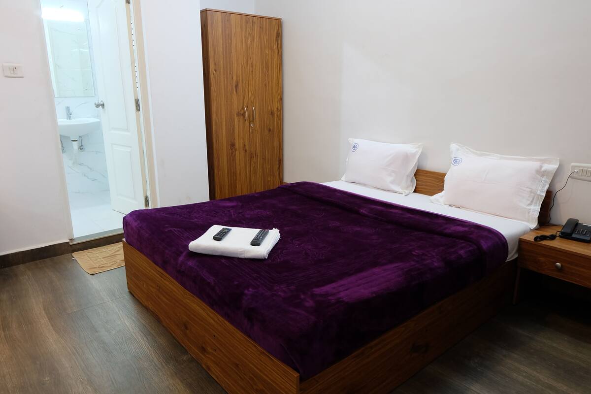 A bedroom with a wooden bed, purple bedding, a white bedside table with a phone, and a wardrobe.