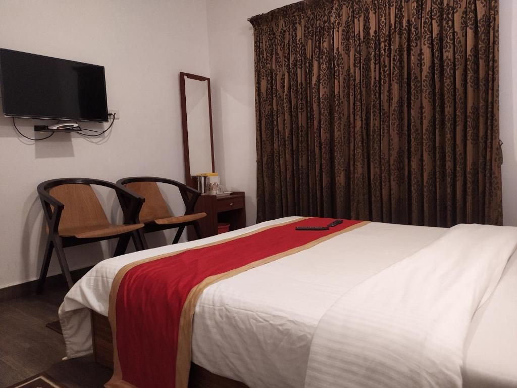 Ein Hotelzimmer mit Bett, einem an der Wand befestigten Fernseher, einem Schreibtisch mit Stuhl und einem großen Fenster mit Vorhängen.