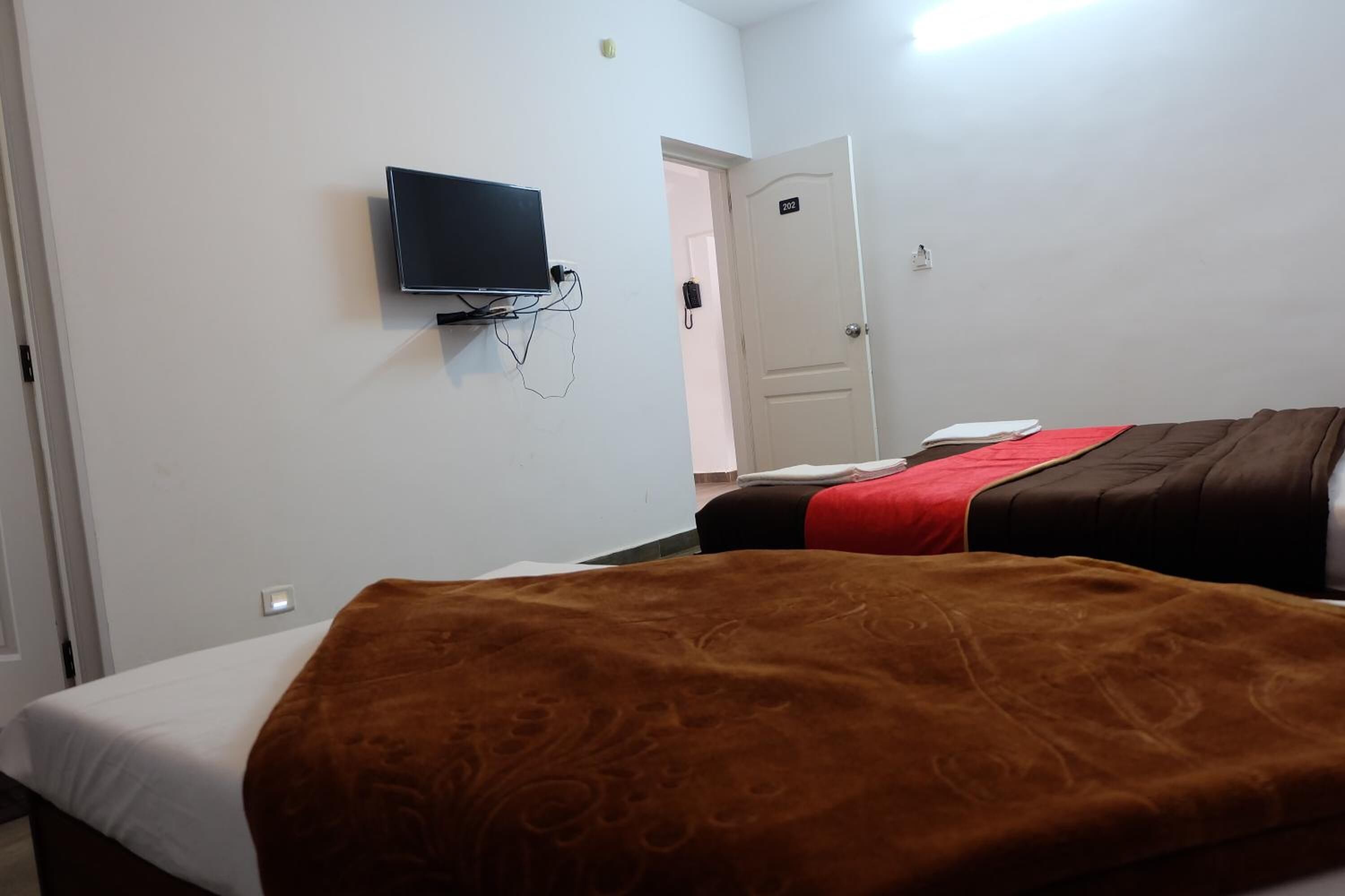 A hotel room with a bed, a television mounted on the wall, and a door with a number.