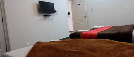 A hotel room with a bed, a television mounted on the wall, and a door with a number.