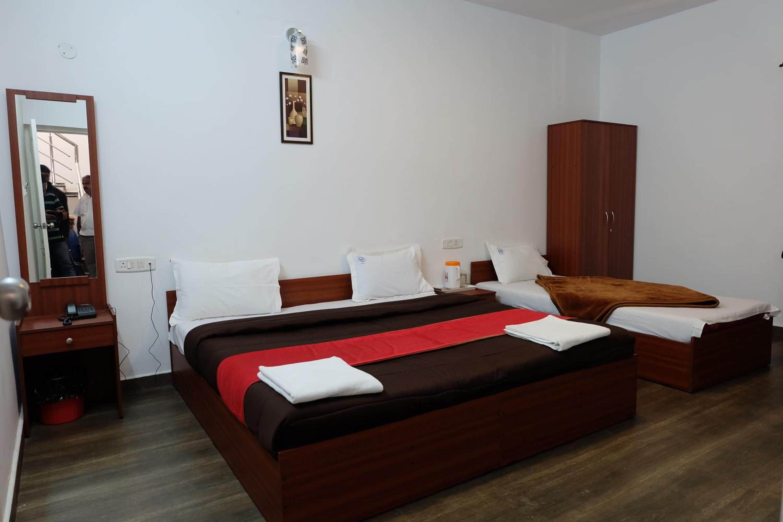 Quarto de hotel com cama grande, guarda-roupa, mesa de cabeceira e espelho.