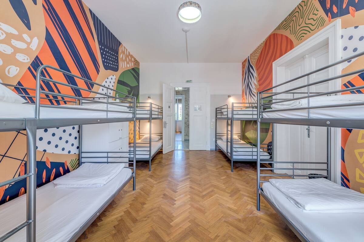 A dormitory room with bunk beds, wooden flooring, and colorful wall art.