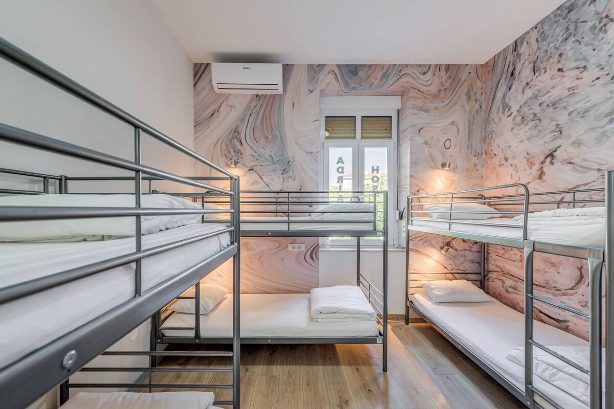 A dormitory room with bunk beds, a marble-patterned wall, and a window with a view.