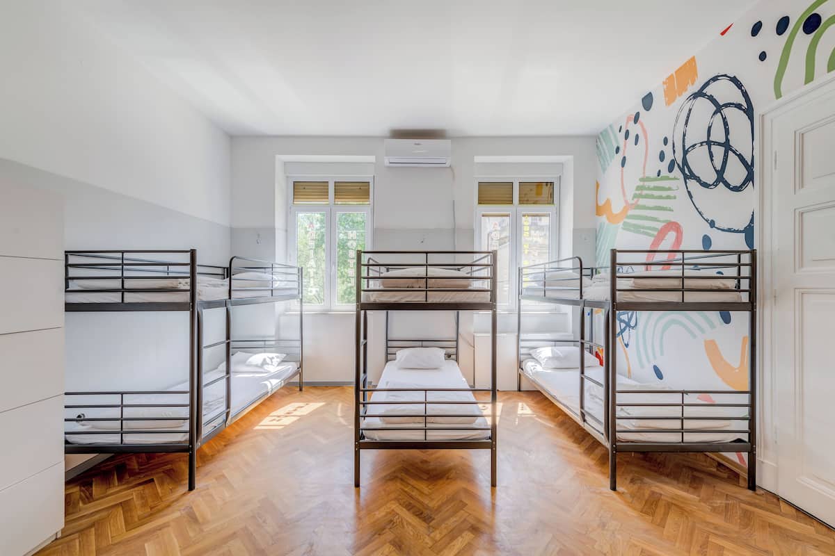 A room with bunk beds, wooden flooring, and a colorful abstract mural on the wall.