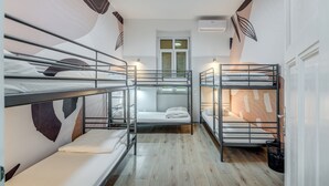 Ein Schlafsaalzimmer mit Etagenbetten, einem Fenster mit Jalousien und einer Klimaanlage.