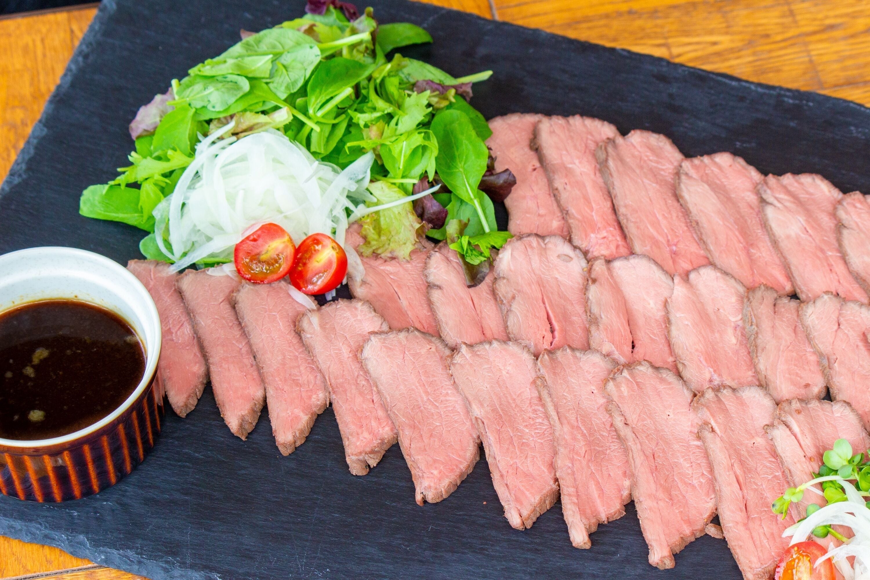 Un plato ordenado con carne cortada en rodajas, una ensalada y salsa para mojar.