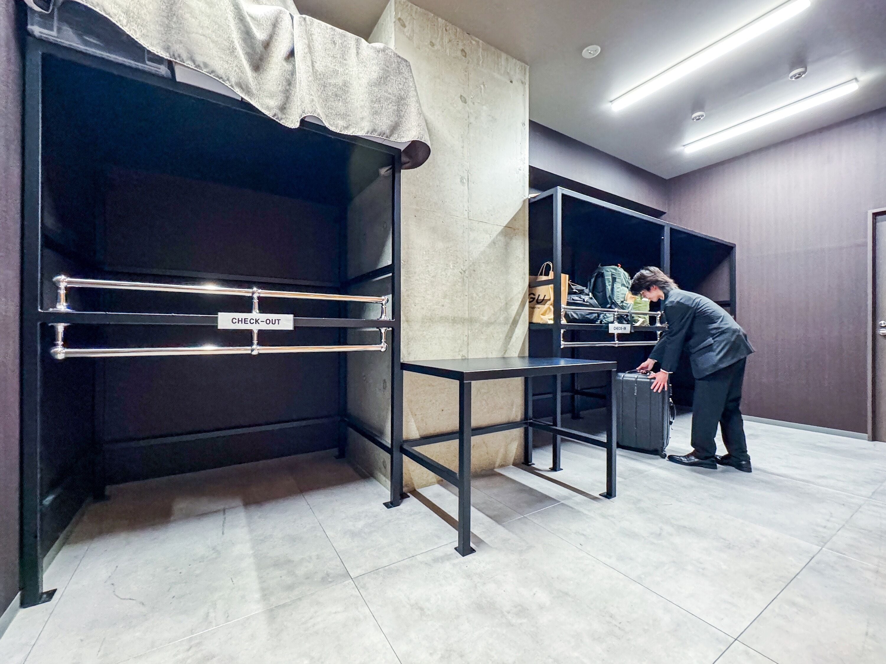 A hotel room with a check-out counter, a bed with a headboard, and a suitcase on the floor.